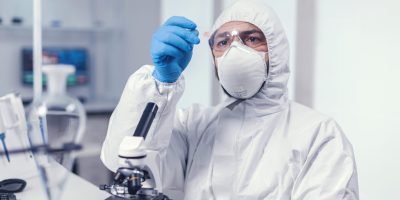 Medical scientist holding a microscope glass slide dressed in ppe during covid19. Examining vaccine evolution using high tech for researching treatment against covid19 virus.